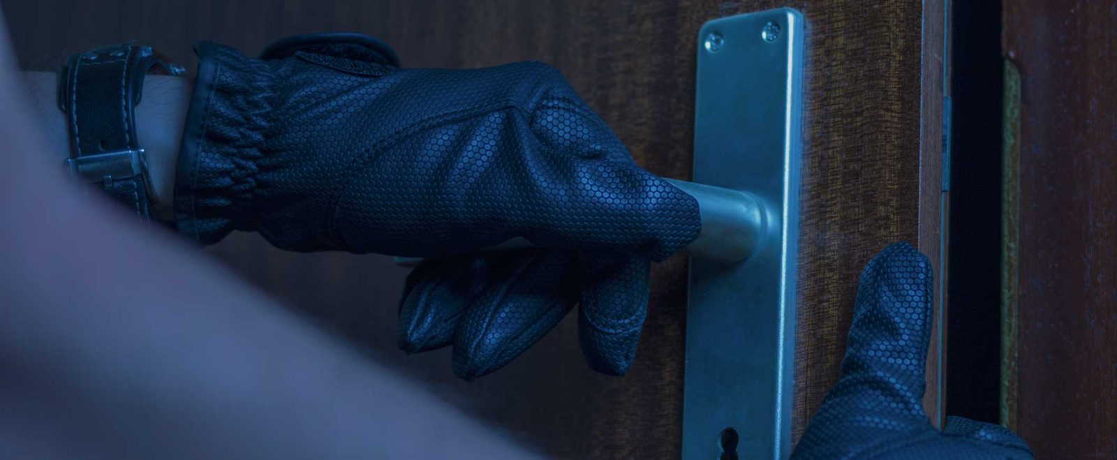 A gloved hand reaching for a door handle in the dark during a burglary