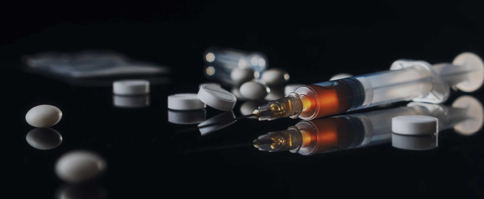 Pills, capsules and a syringe on a dark surface, the evidence behind drug charges