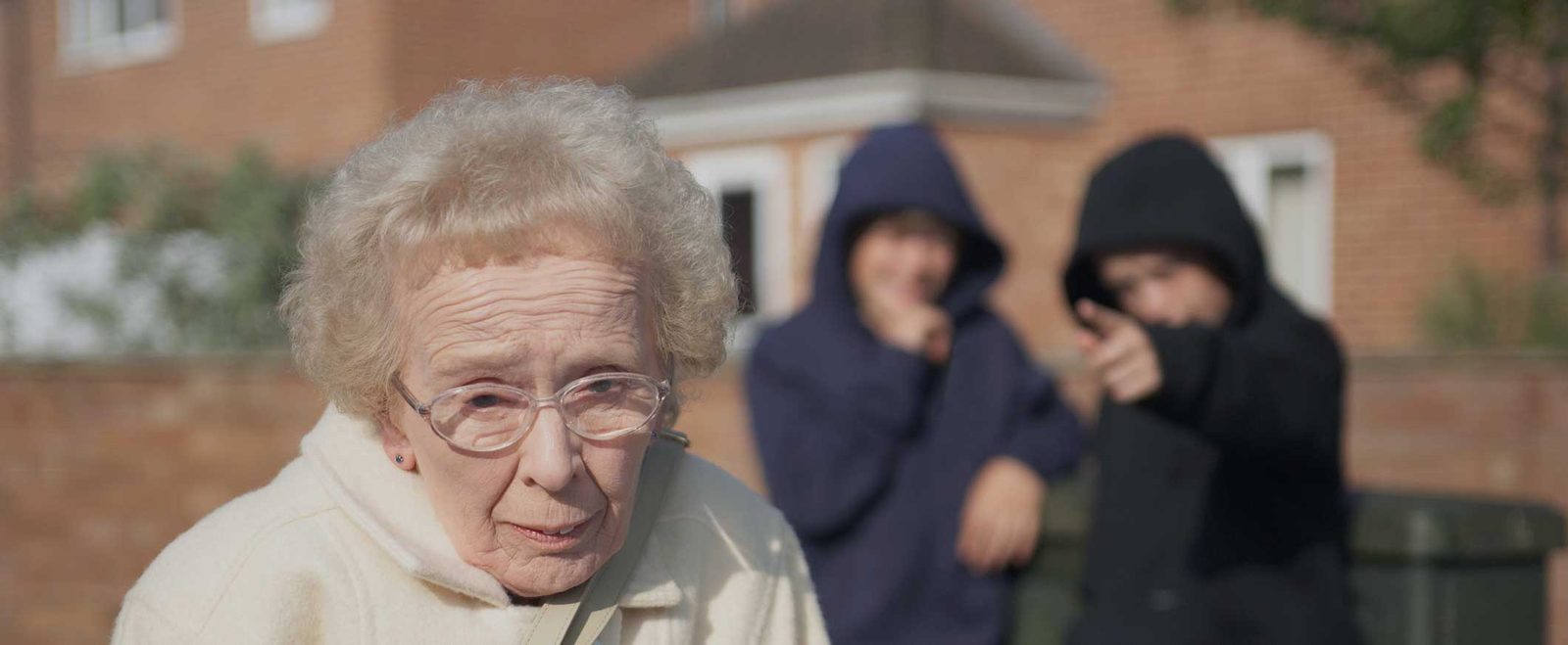 An older woman looking anxious as two hooded figures stand behind her, elder abuse