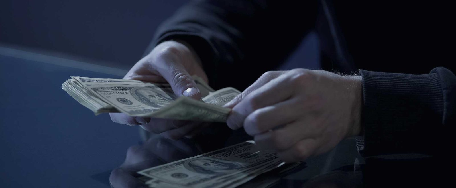Gloved hands counting banknotes in the dark, as in an embezzlement case