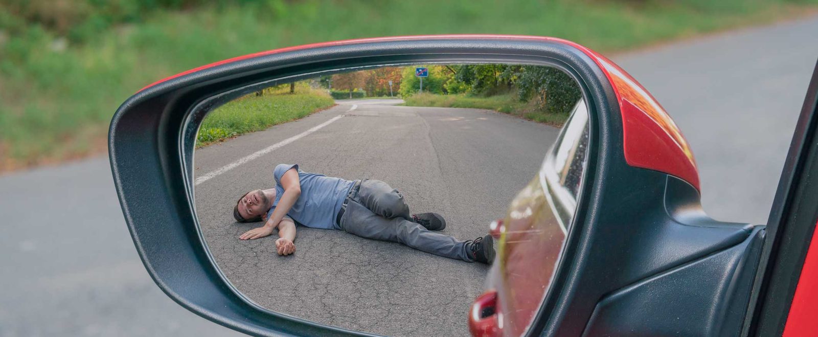 A side mirror reflecting a person lying in the road after a hit and run