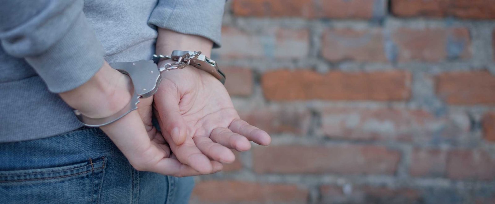 A teenager handcuffed against a brick wall after a juvenile crime arrest