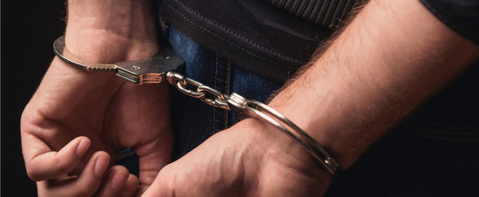 A person's hands being handcuffed behind their back at the start of a criminal defense case