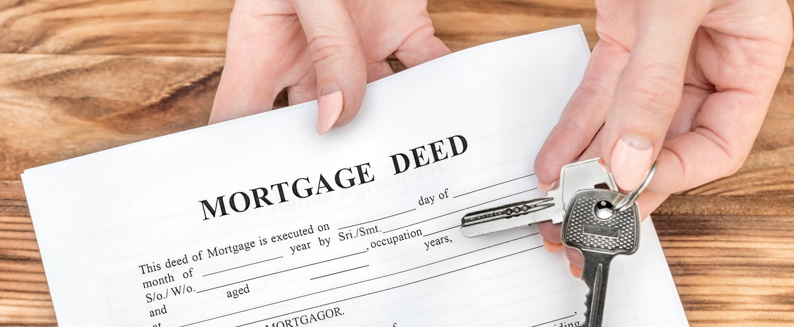 One person handing another a mortgage deed and a set of house keys across a table