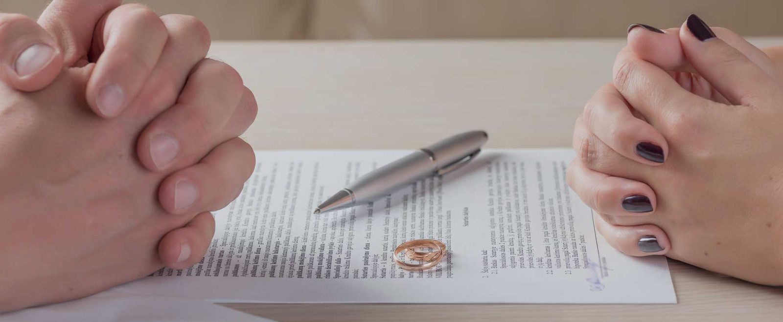 Two people seated either side of a divorce agreement with a wedding ring on the page