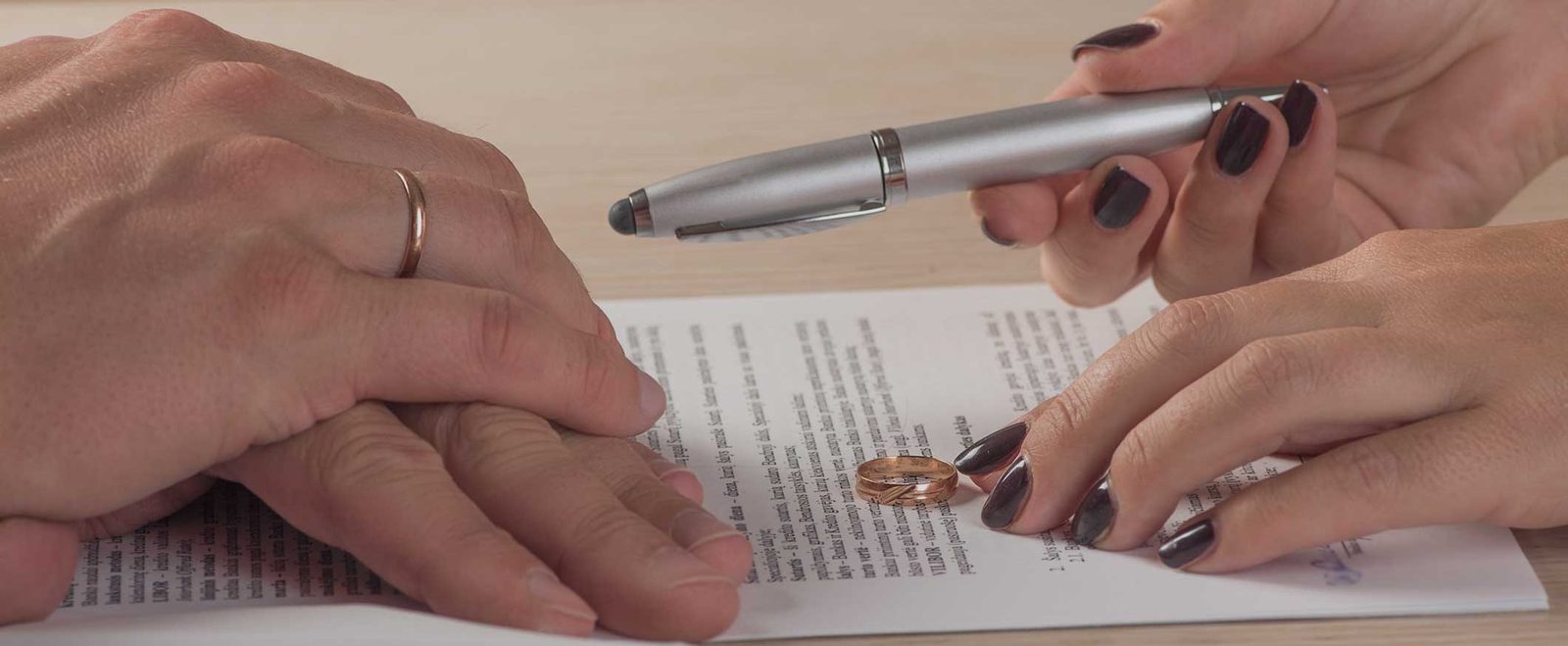 Two people signing a document with a wedding ring on the page during a legal separation