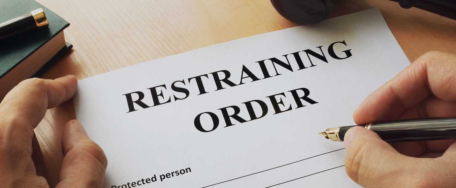 A person signing a restraining order form with a fountain pen