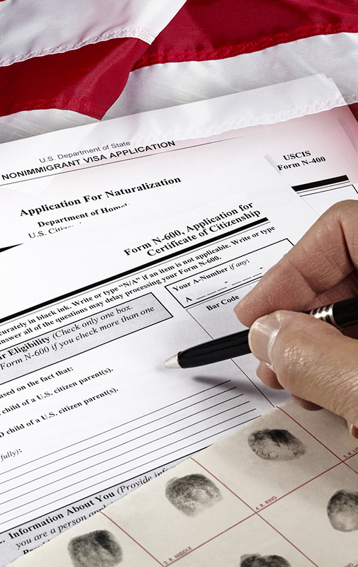 Hands completing a Form N-400 Application for Naturalization in front of a United States flag