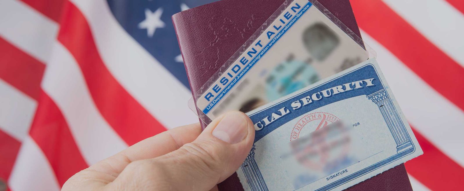 A hand holding a passport, resident card and Social Security card after naturalization