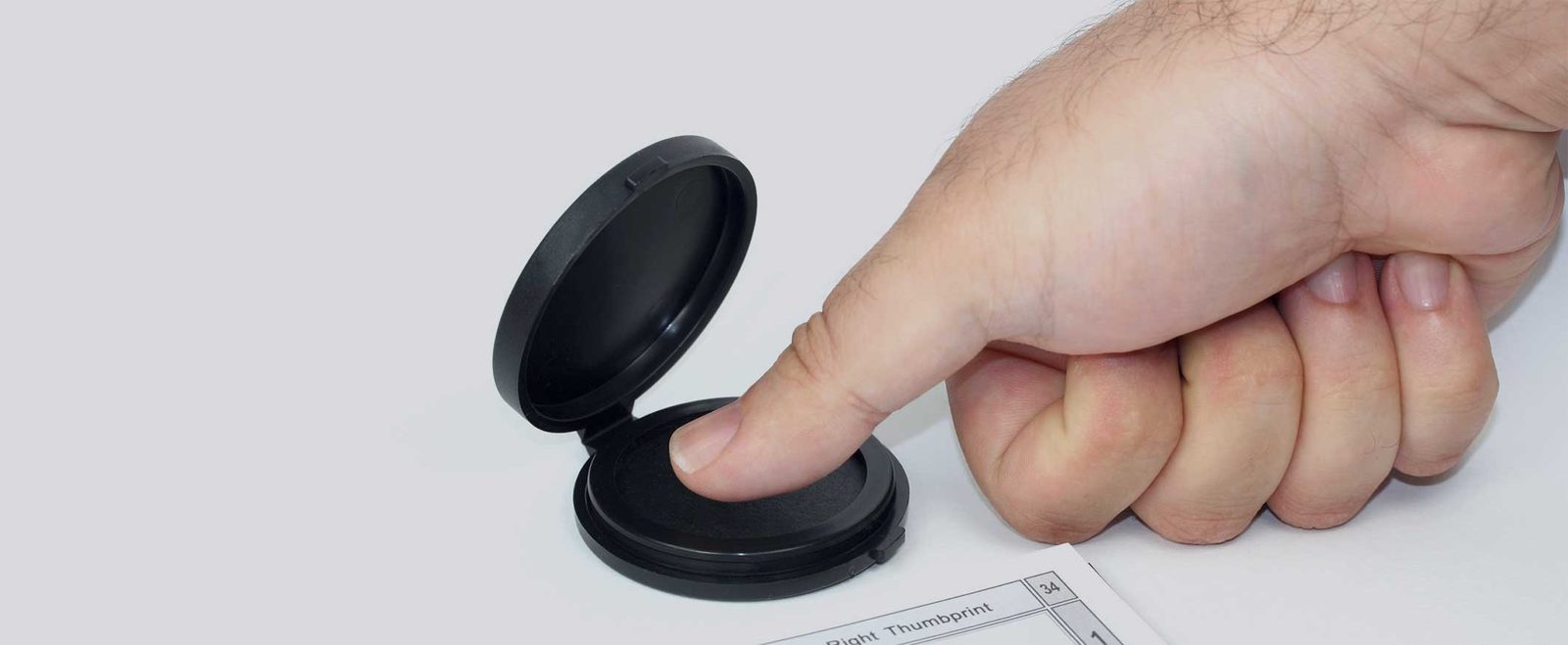 A finger pressed into an ink pad beside a form for a fingerprint background check