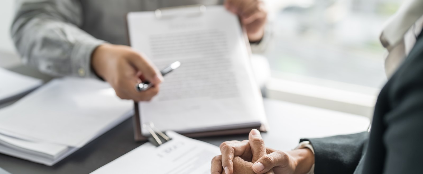 Two people across a desk reviewing legal documents, one holding a clipboard and pen