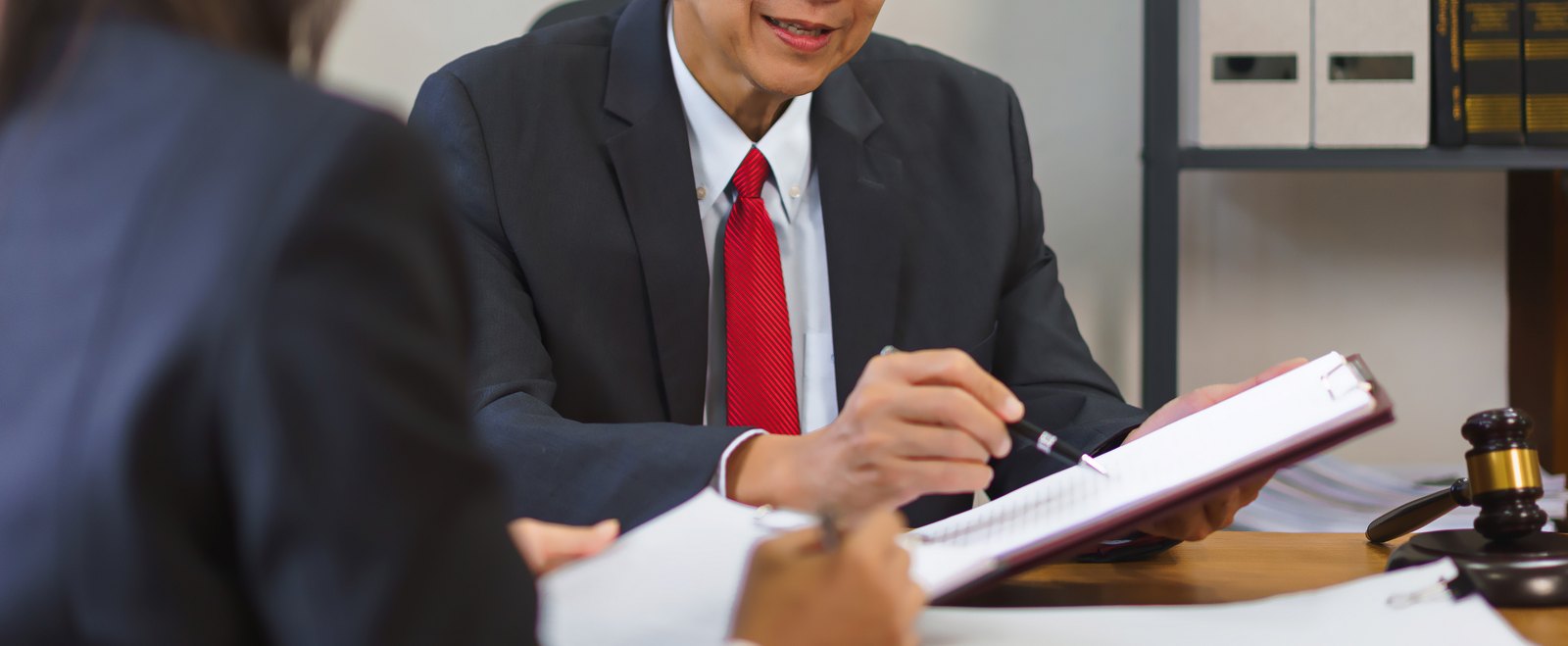 An attorney going through a notepad with a client across the desk, beside a gavel