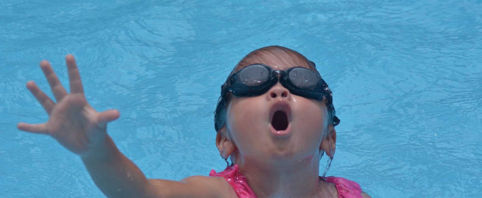 A child in goggles struggling at the surface of a pool during a drowning accident