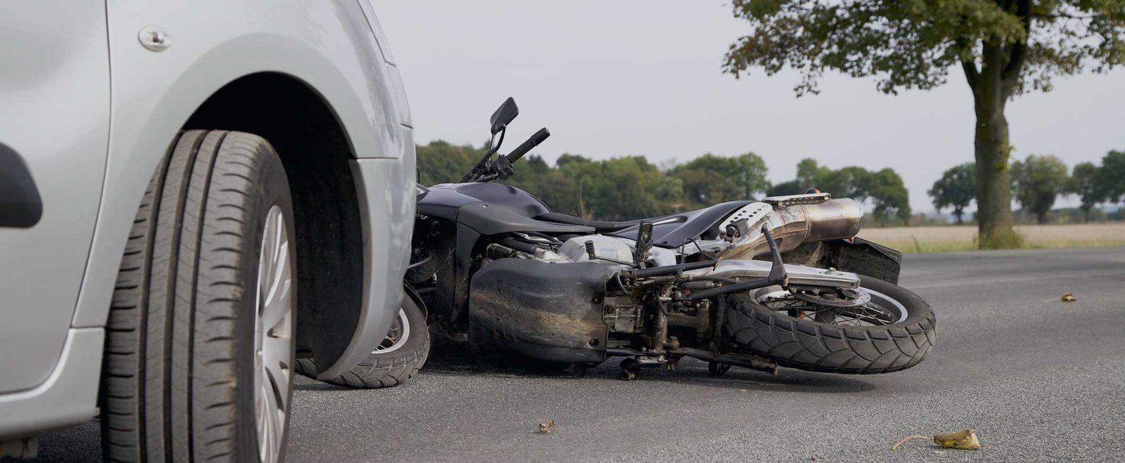 A motorcycle lying on the road beside a car after a motorcycle accident