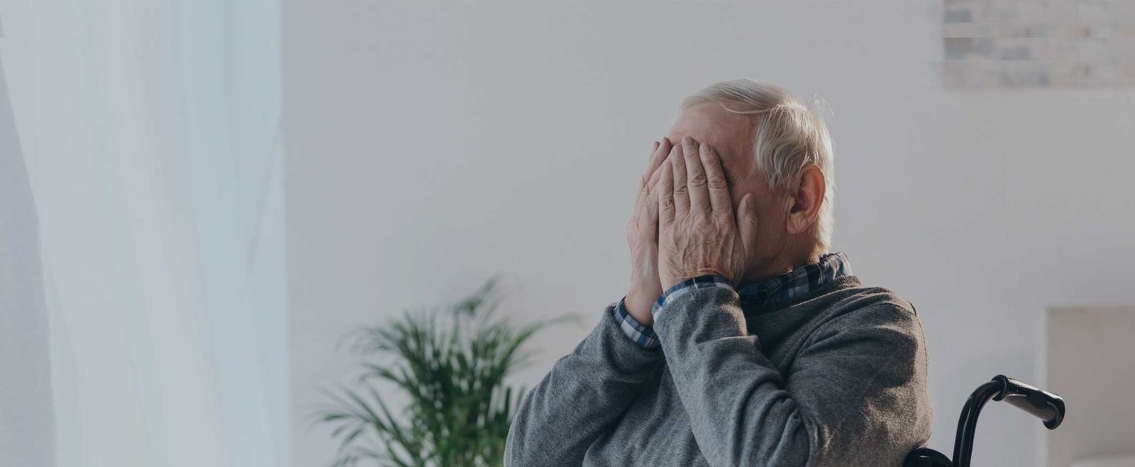 An older man in a wheelchair covering his face, distressed by nursing home negligence