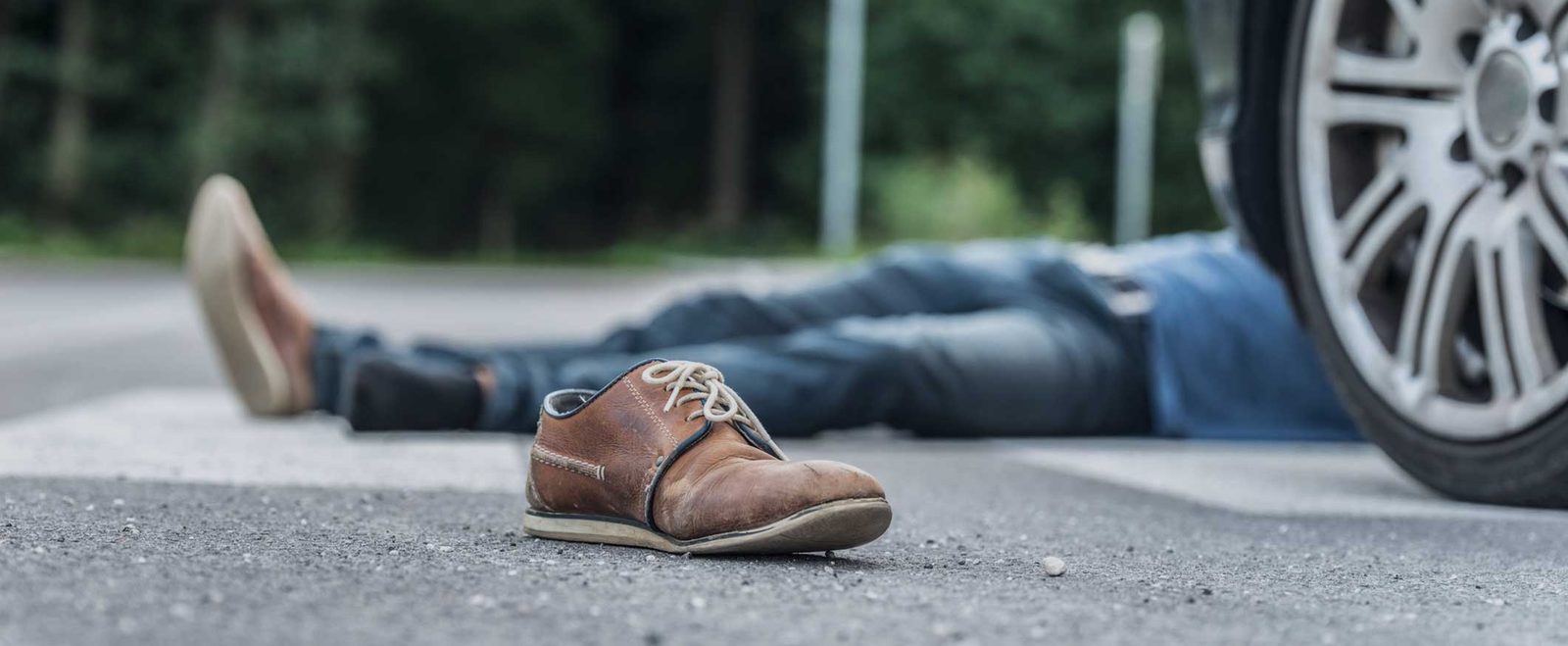 A person lying in the road beside a car wheel after a pedestrian accident