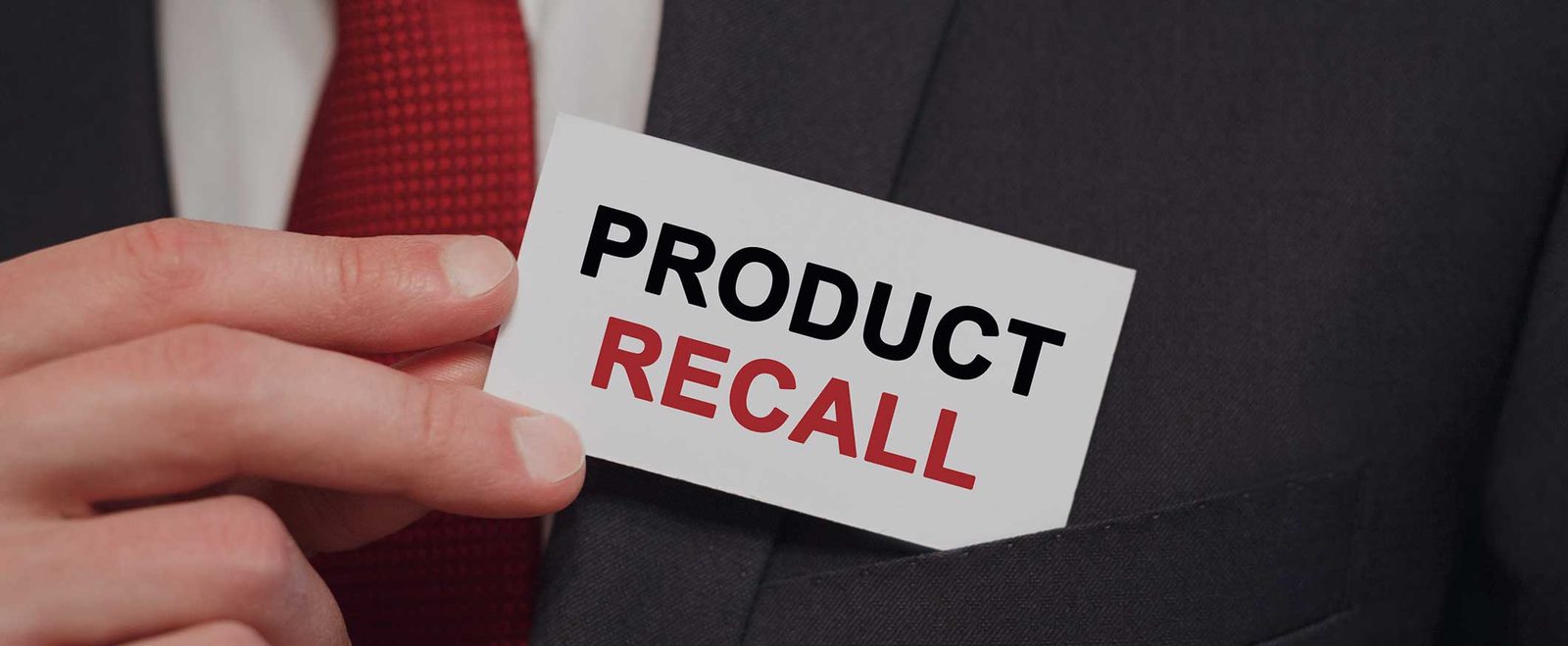 A hand holding a product recall card, the notice that often precedes a product liability claim