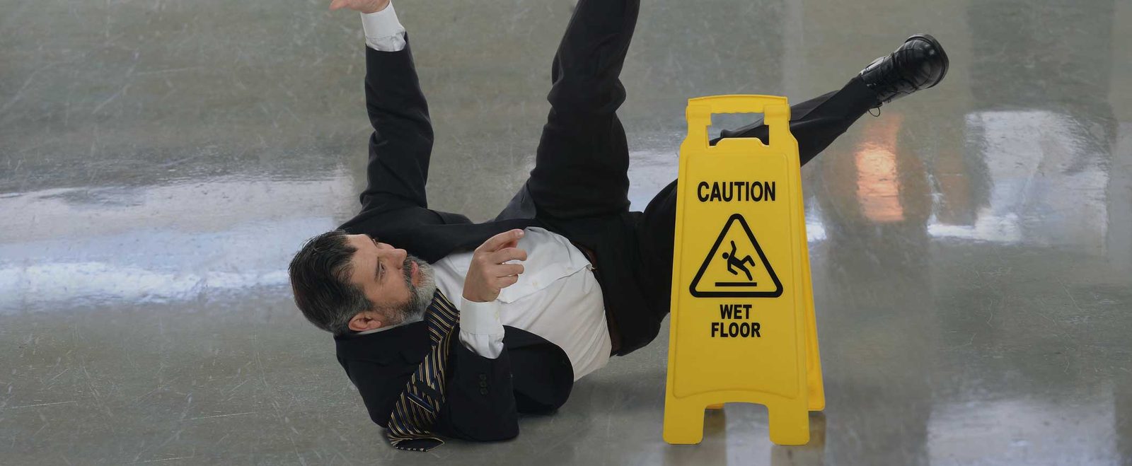 A man falling backwards on a wet floor beside a caution sign, a slip and fall accident