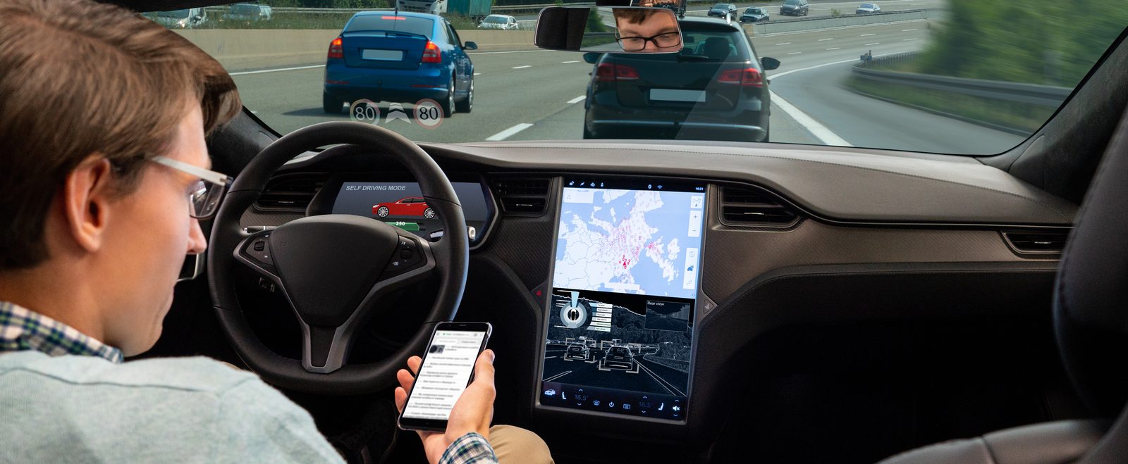 A driver looking at his phone with both hands off the wheel while the car runs in self driving mode