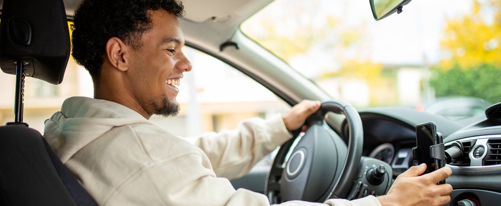 A driver at the wheel reaching for a phone mounted on the dashboard, as a rideshare driver does